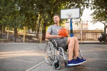 Sporty young man with ball sitting in wheelchair outdoors�