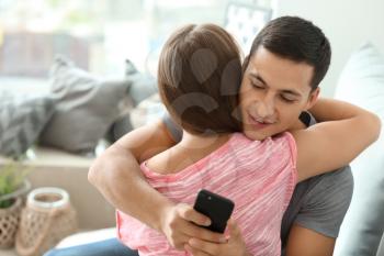 Young cheater texting lover while hugging his girlfriend at home�