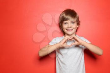 Little boy in t-shirt making heart with his hands on color background�