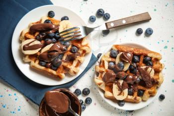 Delicious waffles with banana slices, blueberries and chocolate sauce on light table�