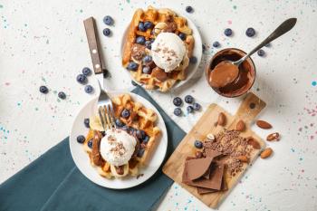 Delicious waffles with banana slices, blueberries and ice cream on light table�