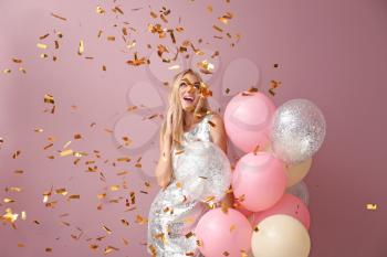 Beautiful young woman with air balloons and falling confetti against color background�