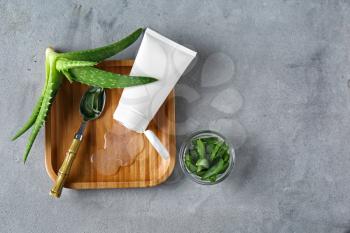 Tube with aloe vera gel and green plant on grey table�