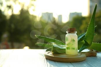 Bottle with fresh aloe vera gel on wooden table outdoors�
