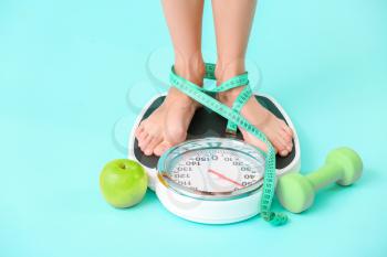 Young woman measuring her weight on color background�
