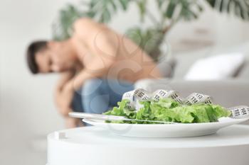 Young man suffering from anorexia and plate with salad at home�