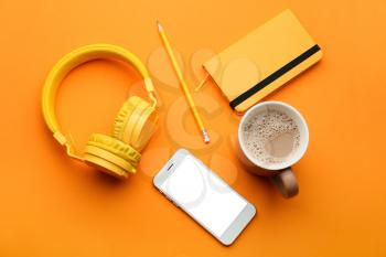 Modern mobile phone with headphones, notebook, cup of coffee and pencil on color background�