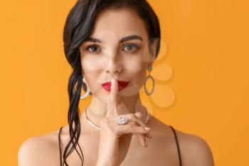 Beautiful young woman showing silence gesture on color background�