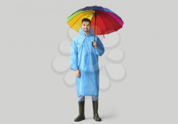 Young man in raincoat and with umbrella on light background�