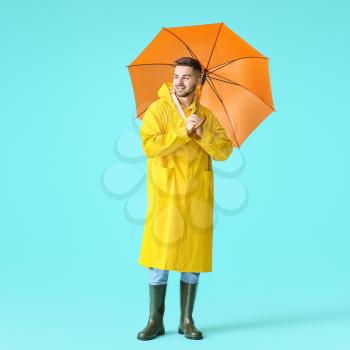 Young man in raincoat and with umbrella on color background�