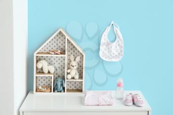 Toys with clothes and baby bottle on chest of drawers in room�