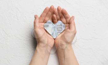 Female hands with origami heart made of dollar banknote on white background�
