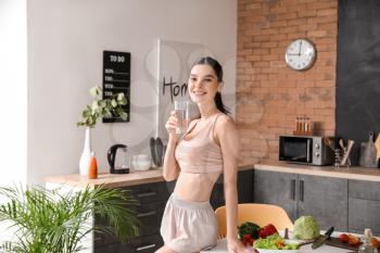 Beautiful young woman drinking water in kitchen�