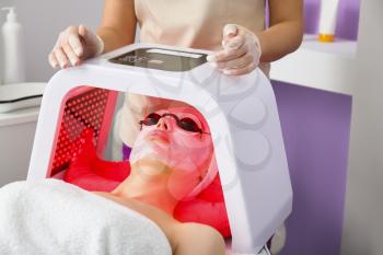 Woman undergoing procedure of facial chromotherapy in beauty salon�