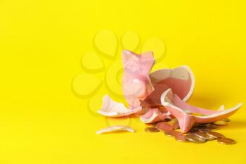 Broken piggy bank and coins on color background�