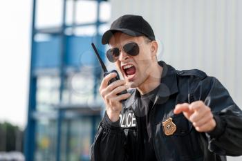 Aggressive police officer with two-way radio outdoors�