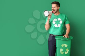 Man in t-shirt with recycling sign, trash bin and megaphone on color background. Ecology concept�