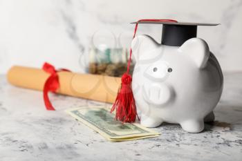 Piggy bank with graduation hat and money on light background�