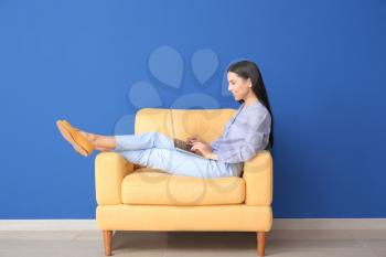 Young woman with laptop relaxing in armchair at home�