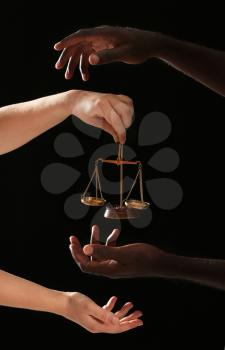 Hands of Caucasian woman and African-American man with scales of justice on dark background. Racism concept�