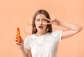 Young woman applying sunscreen cream against color background�