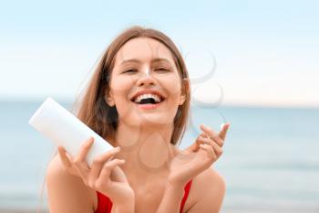 Young woman applying sunscreen cream on sea beach�