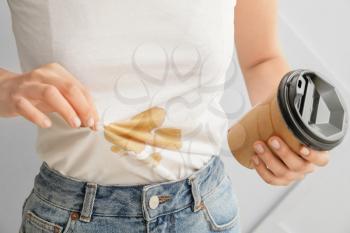Young woman with coffee stains on her t-shirt on light background, closeup�