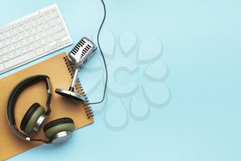 Headphones with microphone, computer keyboard and notebook on color background�