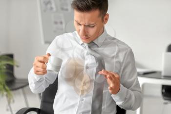 Stressed young businessman with coffee stains on his shirt in office�