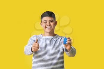 Happy Asian man with car key on color background�