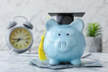 Piggy bank with graduation hat and money on table�