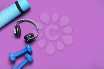Yoga mat, dumbbells and headphones on color background�