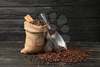 Bag with coffee beans and scoop on dark wooden background�