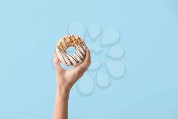Hand with tasty donut on color background�