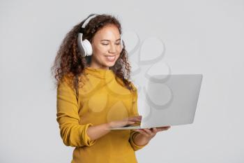 Young woman with laptop and headphones on light background�