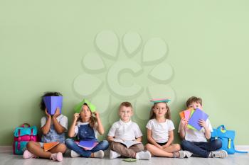 Little children with books sitting on floor against color background�