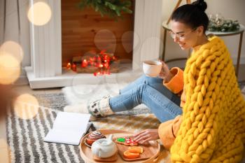 Beautiful young woman with warm plaid reading book and drinking tea at home�