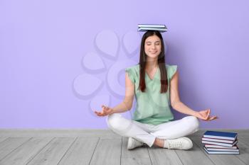 Beautiful young woman with books meditating near color wall�