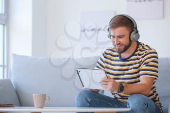 Young man with tablet computer and headphones at home�