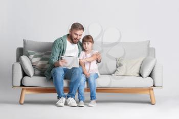 Father and daughter with tablet computer on sofa against light background�