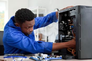 African-American technician repairing computer in service center�