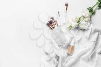 Bottle of makeup foundation, brushes and flowers on light background�