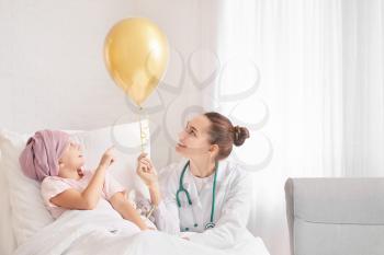 Doctor with golden balloon and little girl undergoing course of chemotherapy in clinic. Childhood cancer awareness concept�