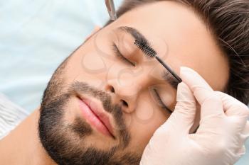 Young man undergoing eyebrow correction procedure in beauty salon�