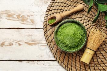 Bowl with powdered matcha tea, scoop and chasen on light wooden background�