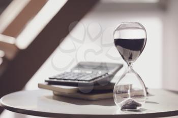 Hourglass, calculator and notebooks on table�