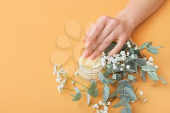 Female hand with jar of cream and beautiful flowers on color background�