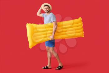 Handsome man with inflatable mattress on color background�