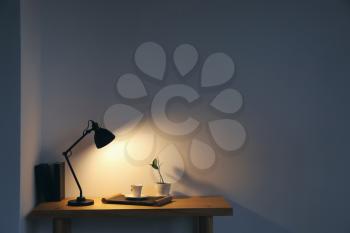 Modern lamp and cup of coffee on table near light wall in room�