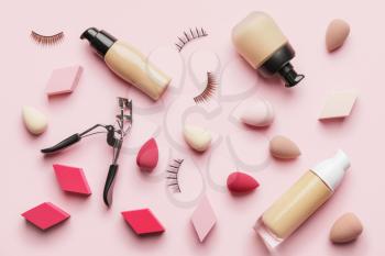 Makeup sponges with tonal foundation and eyelash curler on color background�